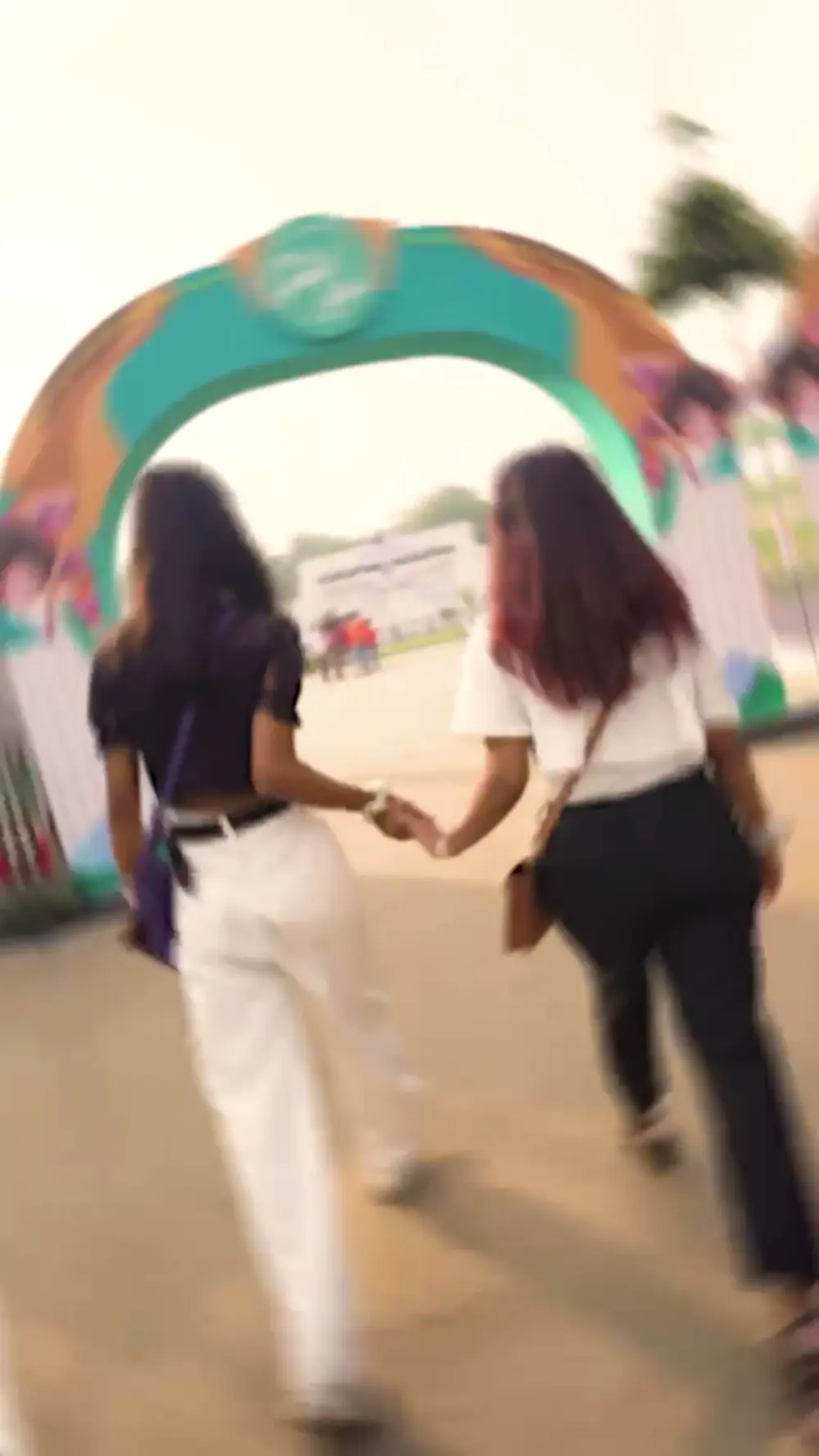 Two friends walking hand in hand under a teal festival entrance arch