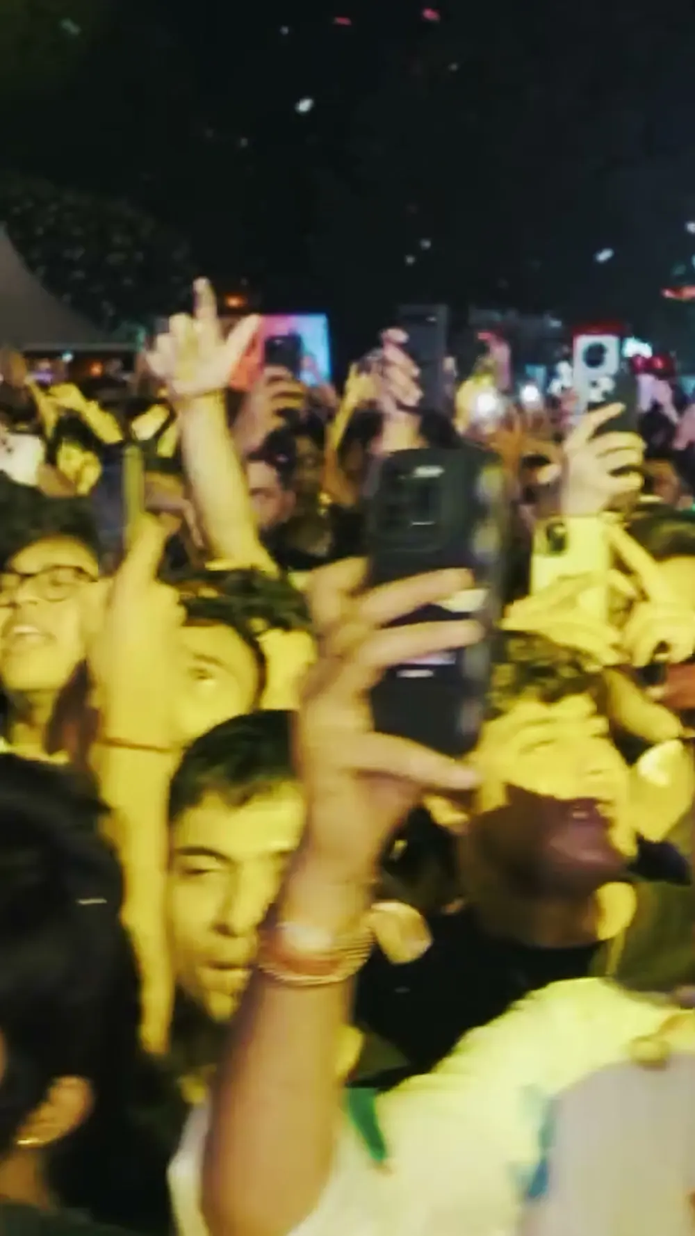 A crowd holding phones up under yellow stage light