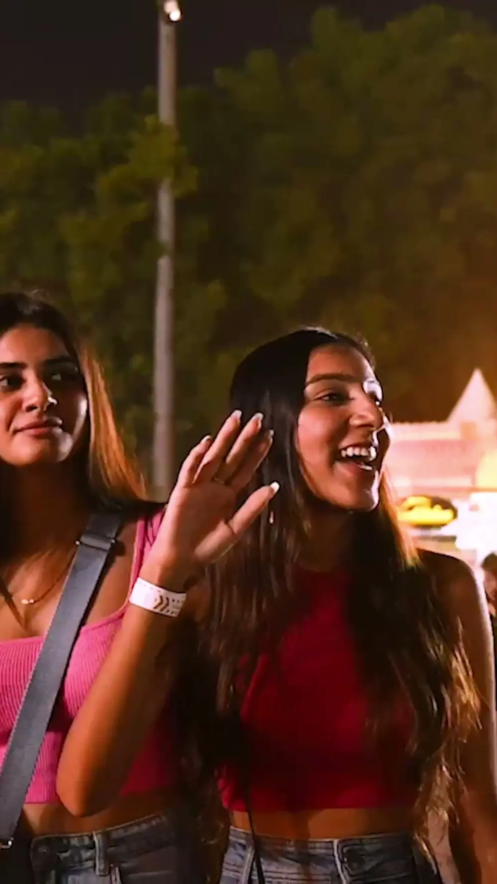 Two women smiling and waving in the crowd at night