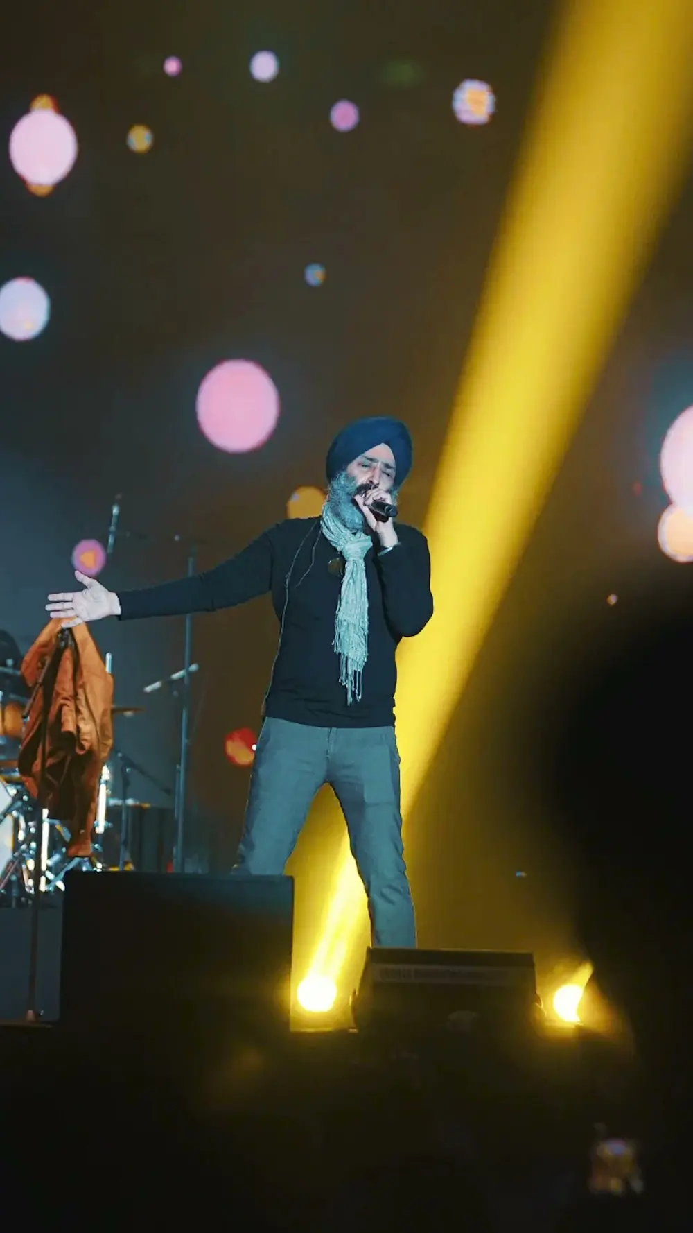 A singer in a turban performing under a yellow spotlight