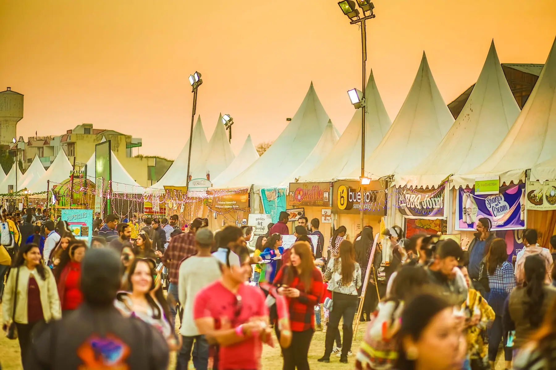 A crowd between white peaked canopies at golden hour